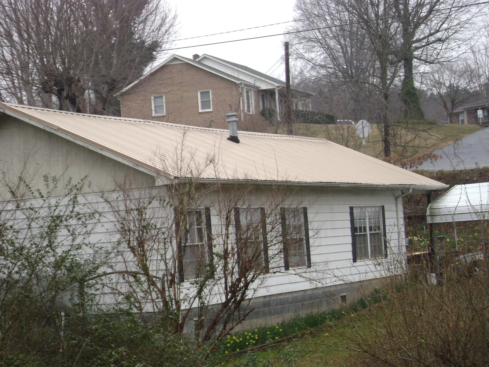 Tan metal roof on a white sided house set into a hillside — Commercial Roofing by Roofing Brothers in Acton
